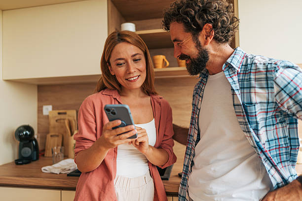 istock Couple using smartphone and smiling in kitchen at home 2227736309