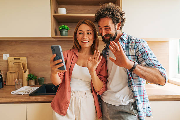 istock Happy couple video calling with family from modern kitchen using smartphone 2227736315