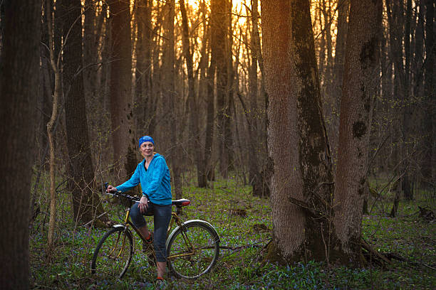 A serene outdoor scene of a woman walking her bicycle along a forest path, surrounded by lush greenery and natural light. The image evokes a sense of tranquility, eco-conscious travel