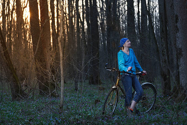 A serene outdoor scene of a woman walking her bicycle along a forest path, surrounded by lush greenery and natural light. The image evokes a sense of tranquility, eco-conscious travel