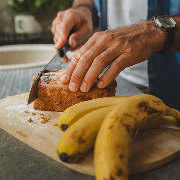 Man slicing freshly baked banana bread on wooden cutting board