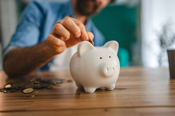 istock Man saving money inserting coin in piggy bank on table 2227743787