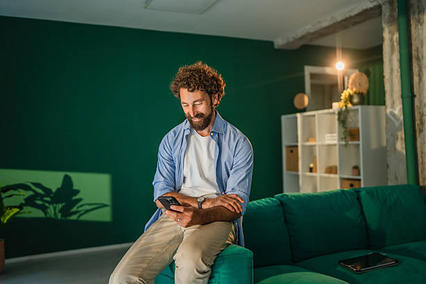 istock Smiling man using smart phone at home sitting on sofa in living room 2227743866