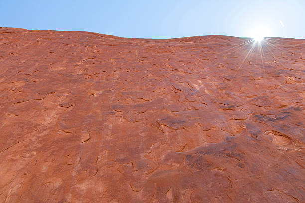Low angle view of steep vertical geological sandstone formation with bright sun and sun rays along Devils Garden Trail in Devil’s Garden district in Arches National Park, Utah, USA