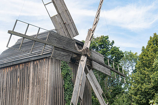 istock Ancient wooden windmill in a rustic, rural setting Weathered structure with outstretched blades, surrounded by lush green trees and clear blue sky Daytime scene with natural lighting No human pres 2227751199