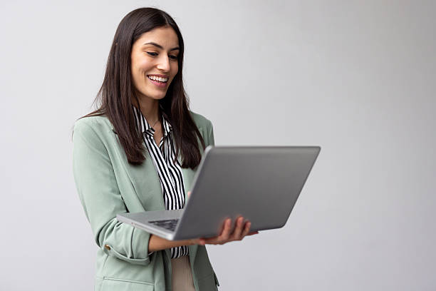 istock Young businesswoman smiling while using a laptop, engaged with the screen, showcasing a sense of joy and professionalism against a white background 2227751827