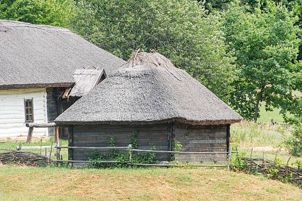 istock Ancient Central European rural structure with thatched roof and gabled design Grass and bare earth ground, wooden fence possible boundary marker Clear sky, bright daylight conditions, no apparent a 2227751914