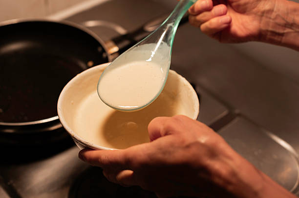A close-up of hands precisely measuring liquid batter with a ladle, ready for frying delicious pancakes. Captures the essential steps of homemade breakfast preparation.