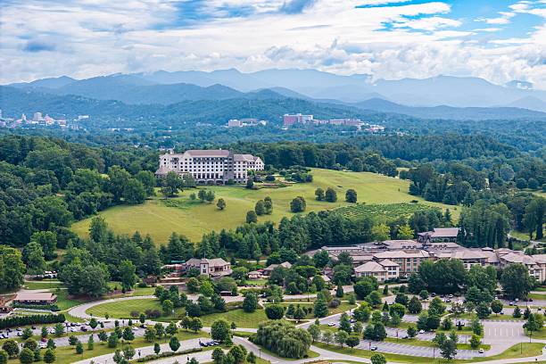 Drone angle view of rolling hills at Biltmore Estate in Asheville, North Carolina with Blue Ridge Mountains and city skyline in background.