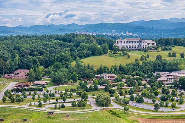 Drone angle view of rolling hills at Biltmore Estate in Asheville, North Carolina with Blue Ridge Mountains and city skyline in background.