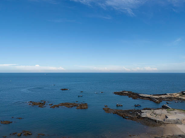 A serene coastal landscape featuring calm blue waters and scattered rocks along the shore, ideal for peaceful imagery or nature-themed projects.