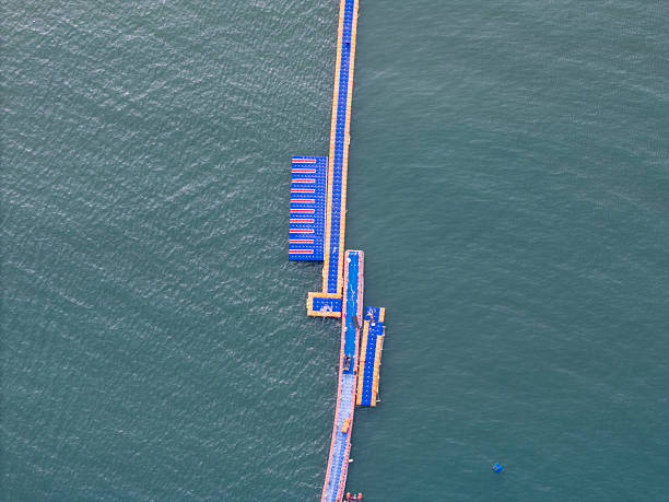 An aerial perspective showcases blue floating structures on water, featuring a long pier-like structure with a small boat nearby. The visual style is modern and industrial, highlighting engineering marvels. Potential usage includes architectural visualization or marine infrastructure documentation.