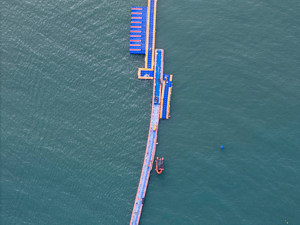 An aerial perspective showcases blue floating structures on water, featuring a long pier-like structure with a small boat nearby. The visual style is modern and industrial, highlighting engineering marvels. Potential usage includes architectural visualization or marine infrastructure documentation.