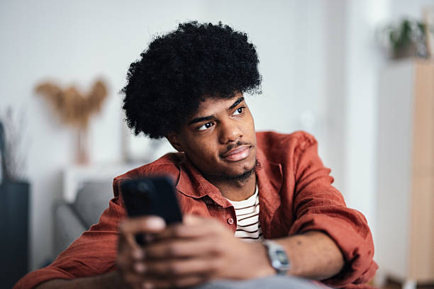 Thoughtful Young Person Relaxing at Home With a Smartphone in Hand