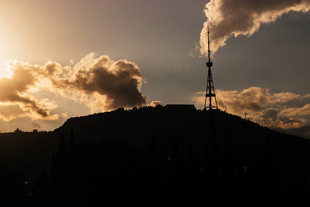 A dramatic sunset behind the Tbilisi TV tower, casting the iconic structure and surrounding forested ridge into silhouette. Captured from below Mtatsminda Hill, the image highlights Georgia’s skyline with glowing clouds and evening hues.