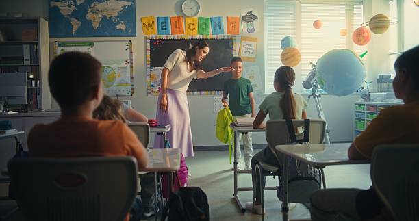 istock Female Teacher Introducing New Young Student in Front of Class Full of Elementary School Children 2227772024