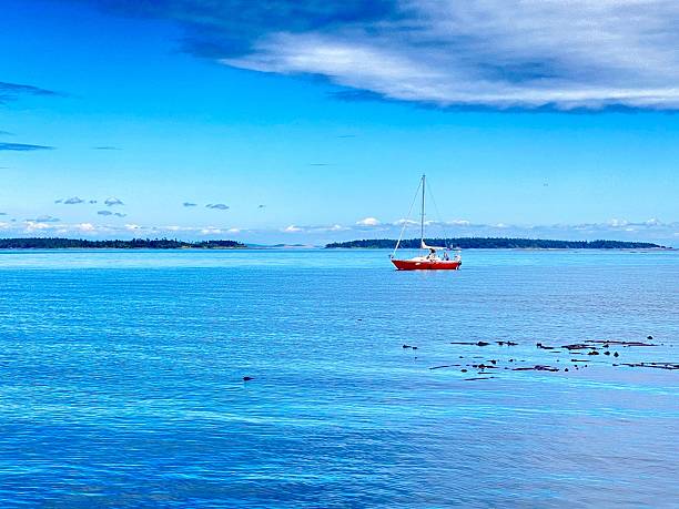A red sailboat on a calm blue sea under a vibrant sky, with distant islands on the horizon.