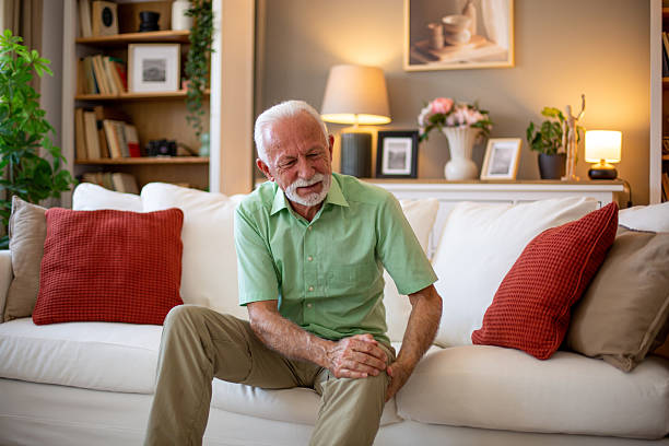 istock Senior man experiencing knee pain while sitting on sofa at home 2227784824