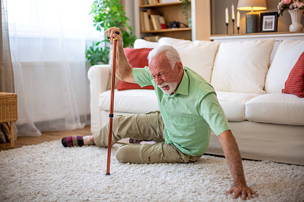 Senior man falling down on carpet at home holding walking cane