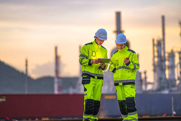 istock Two industrial workers in high-visibility safety uniforms discuss work plans on-site during golden hour, with a refinery or factory plant blurred in the background. 2227784907