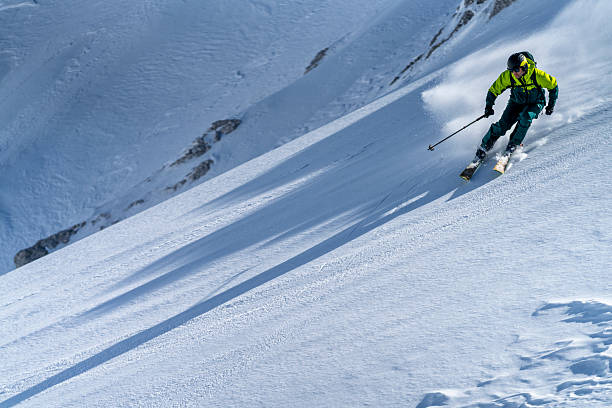istock Athletic Skier In Bright Green Jacket Descending Pristine Snow-Covered Mountain Slope Under Clear Sky 2227788419
