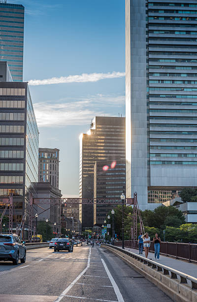 Boston, Massachusetts, USA - July 22, 2025: Incidental people crossing the Summer Street Bridge at sunset. Part of the Federal Reserve Plaza building can be seen on the right of the photo.