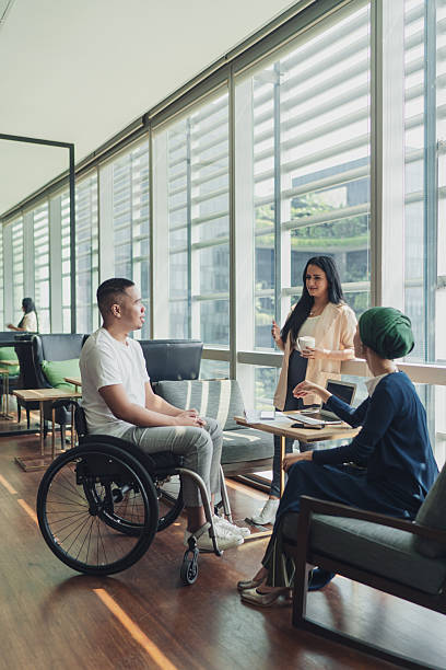 Disabled man in a wheelchair engages with multi racial colleagues at work