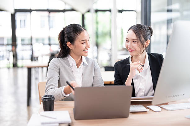istock Two business women sit at desk discuss project details, working on collaborative task, 2227798452