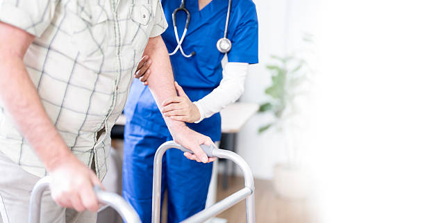 istock Young nurse helping old elderly disable man to walk using walker equipment at home. Senior patient using walking frame with nurse support 2227798490