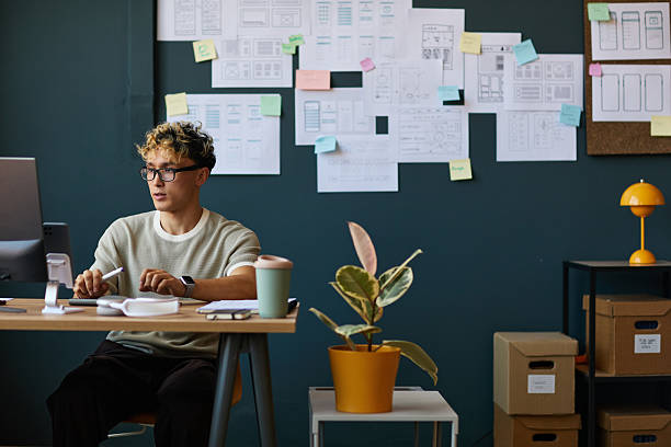 Young Caucasian Man Working at Desk in Modern Office with Design Sketches