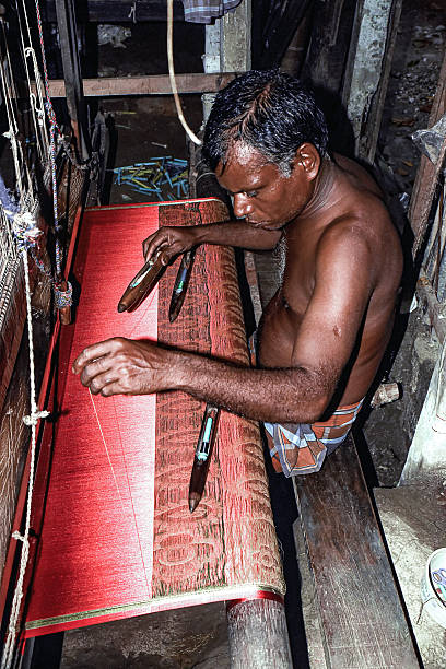 Tangail, Bangladesh - 7 September, 2019: A skilled artisan weaves intricate patterns using vibrant threads in a workshop. Light filters through, highlighting the craftsmanship and dedication involved in textile creation.