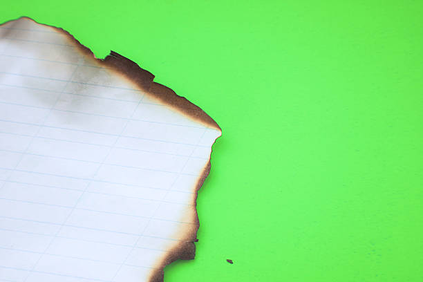 istock A burned sheet of lined paper is placed on a bright green background, creating a distinct visual contrast. The image conveys the concept of destruction, transience, and transformation. 2227810619