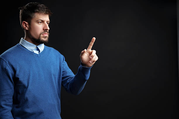 istock Man gestures confidently with one finger raised against a dark background while wearing a blue sweater 2227810929