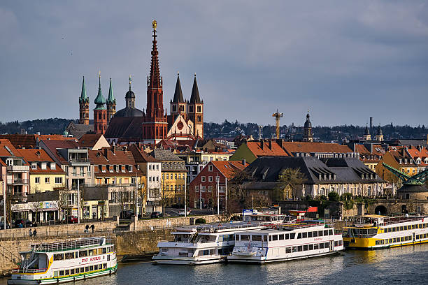 Wuerzburg, Germany - March 29, 2025: Excursion boats on the Main River in Würzburg. To the right is the old crane. In the background the towers of the Mareinkapelle, the Kilinasdom and the Neumünster Church.
