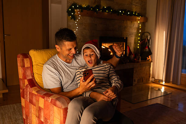 istock Happy father and son having fun while using smart phone at Christmas decorated home in the evening 2227812687