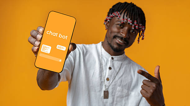 istock Man showcasing chatbot on smartphone against vibrant orange background while smiling and pointing 2227813100