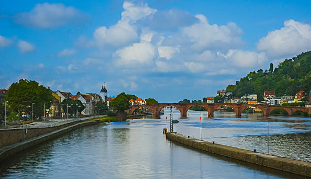 View of the Old Bridge (Alte Brücke) crossing the Neckar River in Heidelberg, Germany, photographed on July 26, 2025. Historic stone bridge with scenic old town buildings and lush green hills in the background.