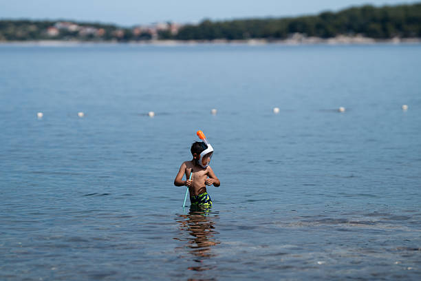 Young boy enjoying summer vacation, happily exploring shallow waters with snorkeling mask and net, discovering marine life under the sun