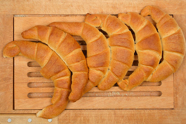 Several freshly baked, golden-brown croissants are arranged on a light wooden cutting board, showcasing their flaky layers