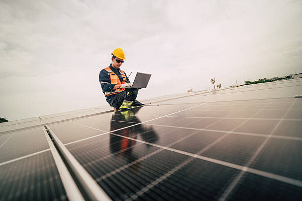 istock Technician works on solar panels while using a laptop on a rooftop in a modern solar energy installation 2227835137