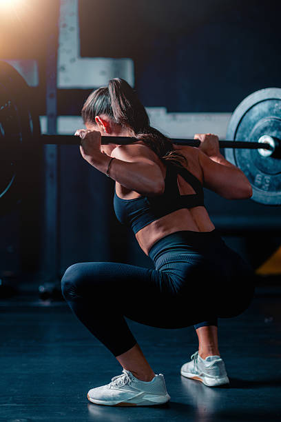 istock Exercising with weights, a woman doing squats uses a barbell and weights for training,  building strength in a supportive gym environment. 2227837356