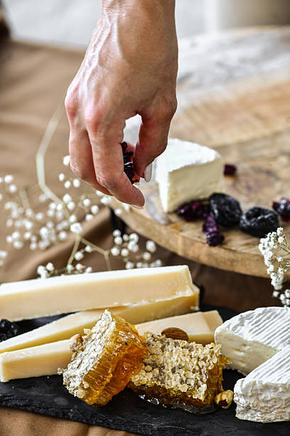 istock Female Hand Adding Dried Fruit On Top Of Cheese Plate 2227845488