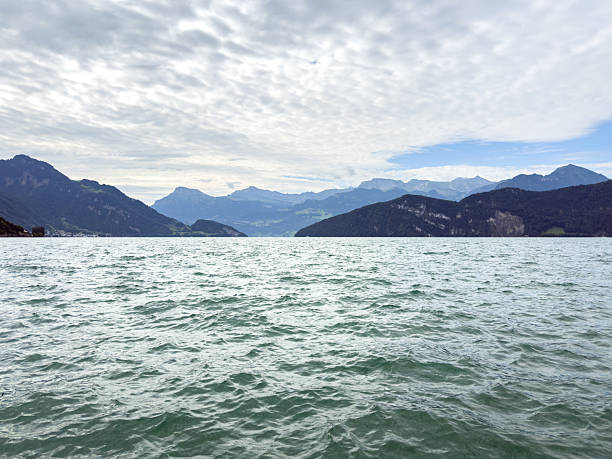 Calm mountain lake with rippling water under a cloudy sky. Scenic view of distant hills and peaks along the shoreline. Nature landscape with water and mountains.