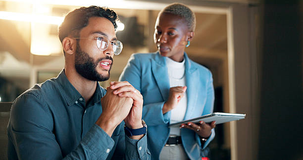 istock Conversation, night and tablet with business people in office together for development or planning. Feedback, problem solving or review with employee man and woman in workplace for project deadline 2227848475