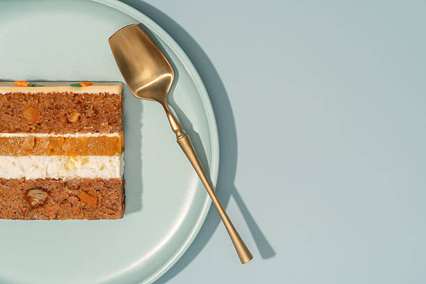 Bento carrot cake slice with orange and mango filling, displayed on a pastel plate with a golden serving spoon, showcasing layers of cake and cream, emphasizing the delightful cross-section