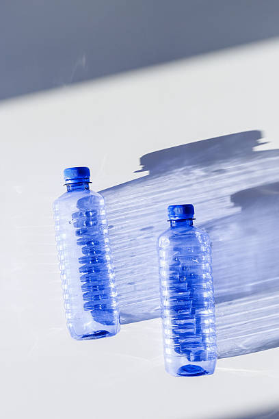 istock Clear plastic water bottles for clean water on white blue background closeup, minimal aesthetic lifestyle photo, top view, flat lay, Naural light, sunlight shadows, caustic light effect, star filter 2227850213