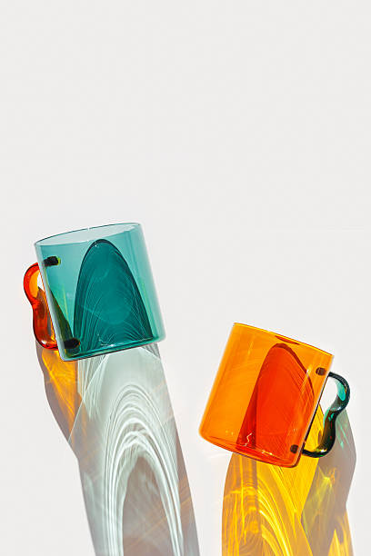 Orange and green Glass Mugs with bright sunlight Shadows, transparent cups casting dynamic, vibrant lights reflections and shadows on light white, creative aesthetic top view, minimal style, closeup