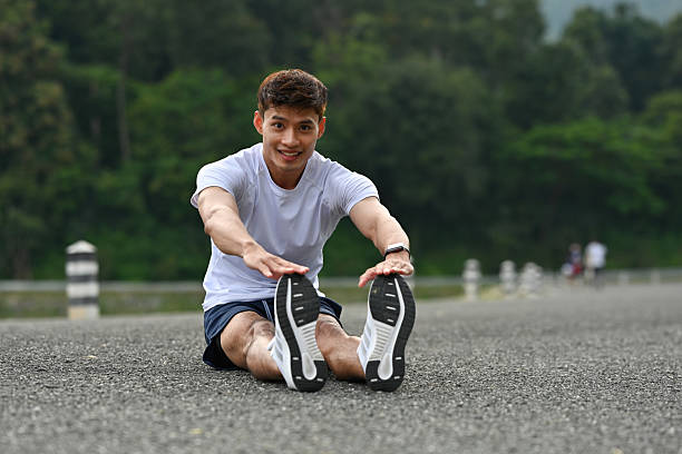 A Fit man sitting on the road performing a forward stretch, preparing for an outdoor workout in a peaceful, natural setting.