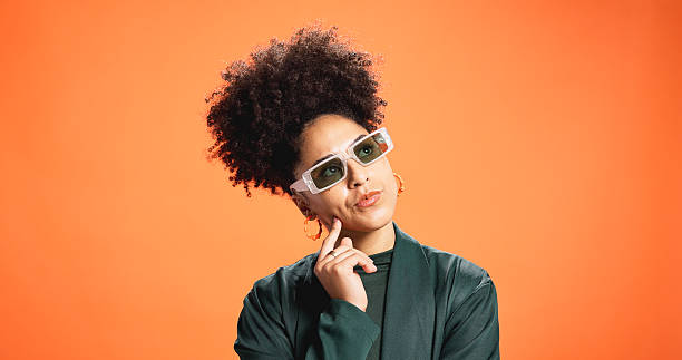 istock Sunglasses, thinking and woman in studio for fashion, reflection or solution on orange background. African person, thoughts and problem solving with idea, wonder or decision for style on mockup space 2227855617