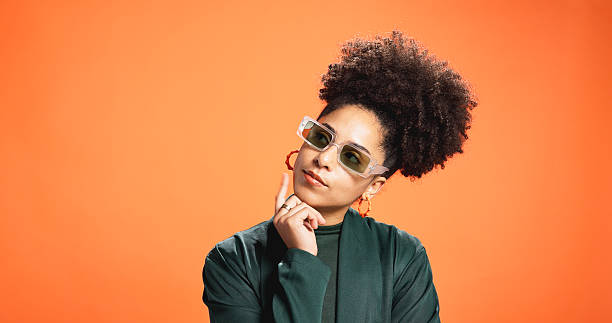 Sunglasses, thinking and woman in studio for reflection, solution or fashion on orange background. African person, shades and thoughts with idea, wonder or decision for cool style on mockup space